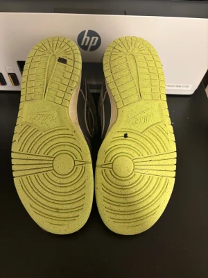 Nike Dunk Low grå/svart med lime sula - Nike Dunk Low sneakers i mörkgrå och svart med slitna detaljer och limegröna sulor. Skorna har snörning, perforerad tå och klassisk Nike-logga på hälen. Ovandelen är i syntet och skinn, med låg profil och platt sula. Perfekt för dig som gillar streetwear och unik stil.