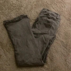 Grå bootcut jeans från Gina Tricot - Snygga ljusgrå jeans från Gina Tricot i storlek 158 (passar mig som är 163 perfekt). Modellen har bootcut-ben och klassisk femficksdesign med dubbla silverfärgade knappar i midjan. Har nästan inget tecken på användning förutom en liten fraktur på ändan av vänstra benet (se på bild). Jeansen är köpta här på Plick. Skriv för mer bilder!