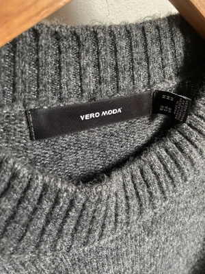 Mörkgrå stickad tröja Vero Moda - Aldrig använd. Mysig mörkgrå stickad tröja från Vero Moda med rund hals och ribbade muddar. Tröjan har lång ärm och slits på sidorna för en chill och loose passform. Perfekt att slänga på sig när det är kallt ute.