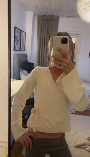 Beige omlottkofta med knyt från Gina Tricot - Superfin beige omlottkofta från Gina Tricot med breda ribbade muddar och knyt i sidan. Koftan har lång ärm och är i mjukt stickat material, perfekt för lager på lager. Snygg v-ringning och croppad passform. Storlek 146-152