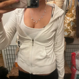 Vit hoodie med dragkedja  - Säljer en vit hoodie med dragkedja framtill, huva med snörning och två fickor. Mjuk bomullskänsla och croppad passform som sitter snyggt på kroppen. Perfekt för en chill och trendig look.