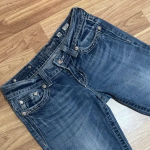 Blå Miss Me jeans med dekorerade fickor - Säljer ett par blå Miss Me jeans med snygga detaljer och dekorerade fickor med nitar och broderier. Modellen har låg midja och bootcut-ben, klassisk tvättad look och coola sömmar. Perfekt för dig som gillar statement-jeans med unik stil. Säljer pga att dom har blivit för tajta, priset kan diskuteras💞