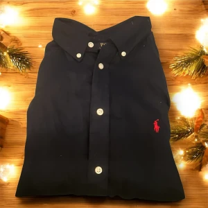 Mörkblå skjorta från Polo Ralph Lauren - Säljer min Ralph Lauren Polo-tröja 👕✨ Passar bäst för personer 165–185 cm (etiketten säger 18–20 år) vilket är köpt från kidsbrandstore. Storlek S, sitter som andra Polo-tröjor.  Tillverkad i lätt linne, perfekt för att hålla sig sval och stilren 👌 Perfekt för dig som vill ha en fräsch och prisvärd Polo-tröja 🔥  Hör av dig om du har några frågor! 😊 