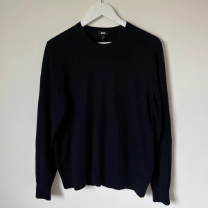 Mörkblå stickad tröja från Uniqlo - Mörkblå stickad tröja från Uniqlo i 100% ull. Klassisk rund hals och långärmad modell med ribbade muddar vid ärmslut och nederkant. Perfekt för dig som gillar enkel och stilren design. 5J13