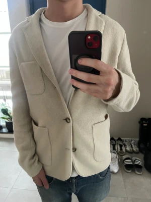 Beige ullkavaj från J.Lindeberg - Snygg beige kavaj från J.Lindeberg i mjuk ull från Lanificio Roma, Italien. Klassisk design med två stora fickor fram, knappar och krage. Perfekt för dig som gillar stilrena och tidlösa plagg med en modern touch. Nypris 3599kr mitt pris 1099kr. Varan är endast använd en gång. 