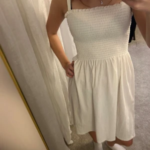 Vit smockad sommarklänning - Supersöt vit klänning med smockad överdel och axelband. Kjolen är lätt utställd och har en mjuk, flowy känsla. Perfekt för varma dagar och har en fräsch, ljus look. Materialet känns som bomull och är riktigt bekvämt mot huden.