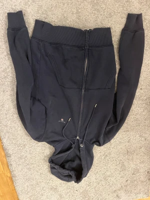 Svart hoodie från GANT med dragkedja - Svart hoodie från GANT i storlek S med huva och snörning. Tröjan har en hel dragkedja framtill, två fickor och ribbade muddar vid ärmslut och nederkant. Perfekt för chill dagar och enkel att matcha med jeans eller joggers.