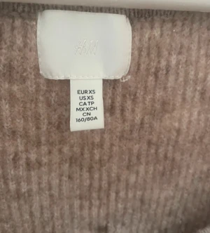Beige stickad långärmad tröja H&M - Säljer en beige stickad tröja från H&M i storlek XS. Tröjan har en snygg v-ringad hals och ribbad struktur som ger en schysst look. Långärmad och i mjukt material som passar perfekt när det är lite kyligare ute.