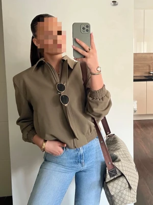 Olivgrön bomberjacka från Zara - Snygg olivgrön bomberjacka från Zara med klassisk krage och elastiska muddar vid ärmslut och midja. Materialet är mjukt och lätt, vilket gör den skön att bära. Ny med prislapp!! 