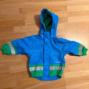 Blå regnkläder(fodrad) från Didriksons barn. Strl 70 - Säljer ett par blå regnbyxor samt regnjacka från Didriksons med gröna och grå detaljer. Byxorna har förstärkta knän, reflexband runt benen och justerbara axelband i grön fleece. Perfekta för utelek under kalla dagar. Strl 70 men stora i storlek.