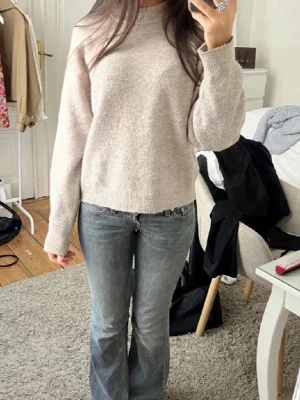 Beige stickad tröja med lång ärm - Säljer en enkel och snygg beige stickad tröja med rund hals och långa ärmar. Tröjan har en mjuk och lite fluffig känsla, perfekt för att hålla sig varm under kyliga dagar. Passar dig som gillar en clean och chill stil.