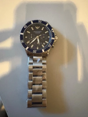 Armani klocka! 100meter  - Bilderna visar en klocka från Emporio Armani med blå urtavla och silverfärgad länkarmband i metall, men ingen väst finns med. Blå! 