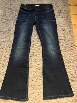 Bootcut jeans i mörkblå denim - Snygga bootcut jeans i mörkblå denim med klassiska fickor fram och bak. Jeansen har en markerad söm och bredare benslut som ger en cool siluett. Perfekta för dig som gillar retrovibbar och vill ha ett par jeans med lite extra attityd.