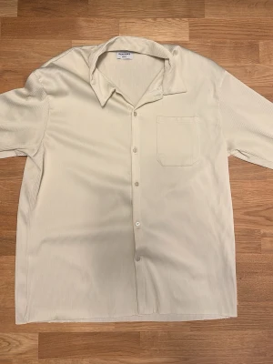 Beige skjorta från Jack & Jones XL - Säljer en beige skjorta från Jack & Jones i storlek XL. Skjortan har diskreta ränder, klassisk krage, kort ärm och en bröstficka. Tillverkad i ett mjukt material som känns skönt mot huden. Perfekt för dig som gillar stilrena plagg.
