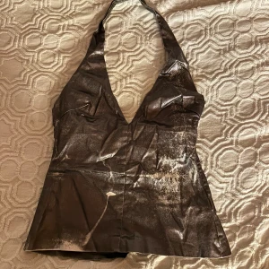 Glittrig silvrig halterneck topp från Zara - Säljer en snygg silvrig halterneck topp från Zara i storlek S. Toppen har glittriga detaljer och en djup v-ringning framtill. Materialet är syntet och ger en cool metallic-look. Perfekt för dig som vill sticka ut med en trendig och unik topp.