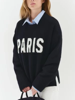 Mörkblå stickad tröja med PARIS-tryck - Säljer en mörkblå stickad tröja med stort vitt PARIS-tryck framtill. Tröjan har en loose passform, långa ärmar och är lite öppen vid tröjans slut. 