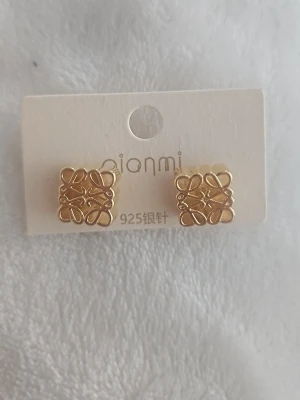 Örhängen - Bilderna visar ett par guldfärgade örhängen från Qianmi, inte en väst. Örhängena har ett fyrkantigt format med dekorativa detaljer.