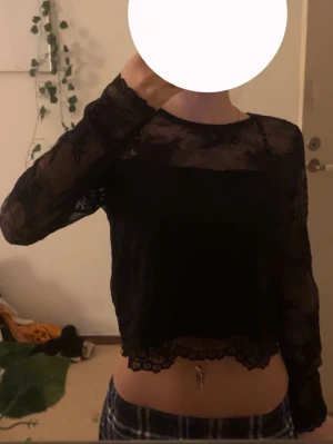Svart spetsblus med lång ärm - Säljer en svart blus i transparent spets med lång ärm och rund hals. Blusen är croppad och har fina spetsdetaljer vid nederkant och ärmslut. Perfekt för dig som gillar en lite edgy och feminin stil.