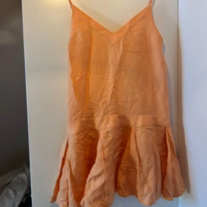 Sommrig aprikosfärgad linneklänning med volang från Nakd med band och detaljer  - Helt ny med pris lapp , nypris 500kr Säljer en aprikosfärgad kort klänning i linneblandning med v-ringning och smala axelband. Klänningen har en volangkant nedtill som ger en flowy känsla. Perfekt för varma dagar och enkel att styla med smycken eller en jeansjacka.