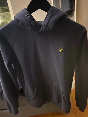 Lyle & Scott Hoodie Mörkblå  - Snygg blå luvtröja med cool design på snören. Är i helt nyskick, inga fläckar eller slitage. Skriv för fler bilder. Storlek för 14/15 år (XS-S).