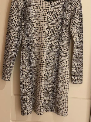 Svartvit mönstrad långärmad klänning - Säljer en svartvit klänning med unikt rutigt mönster. Klänningen har lång ärm och rak passform, perfekt för dig som gillar grafiska prints. Materialet känns mjukt och stretchigt, vilket gör den bekväm att bära. Snygg till sneakers eller boots.