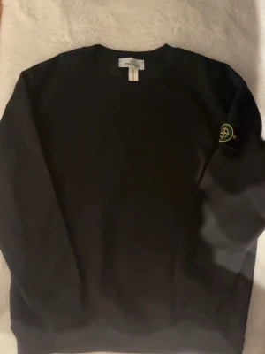 Svart sweatshirt från Stone Island - Svart långärmad sweatshirt från Stone Island med klassisk rund hals och ikonisk patch på vänster ärm. Tröjan är i mjuk bomull och har en clean look som passar perfekt till streetwear. Märkesetikett och certifikat för äkthet medföljer.
