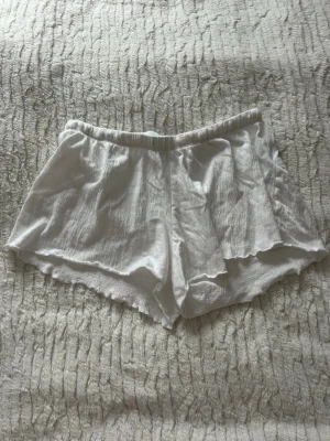Vita loose shorts från 157 - Säljer ett par vita, loose shorts från 157 i storlek S. De har elastisk midja och är gjorda i ett mjukt, krinklat bomullstyg som känns chill och luftigt. Perfekta för varma dagar och har en enkel, clean look med vågiga kanter.