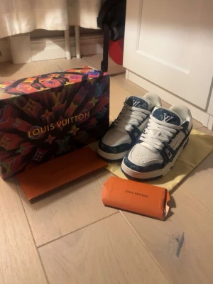 Louis Vuitton blåvita sneakers - Säljer ett par Louis Vuitton sneakers i blått och vitt med klassiskt LV-monogram och detaljer i skinn. Skorna har rund tå, platt sula och snörning. Kommer med originalkartong och dustbag. Snygg design med tydliga Louis Vuitton-loggor på både ovansida och sula.