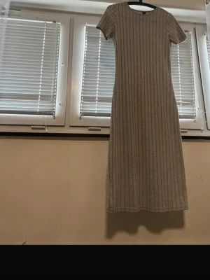Ribbed Knit Midi Dress – Short Sleeve – Neutral Beige/Grey - Minimalist ribbed knit midi dress in a neutral beige/grey tone. Soft, stretchy fabric with a flattering straight fit. Short sleeves and a simple round neckline make it perfect for everyday wear or dressing up with accessories. Easy to style for all seasons – wear it with sneakers for a casual look or boots and a jacket for autumn/winter. ✔ Comfortable & stretchy ✔ Timeless, minimalist style ✔ Great condition, no flaws Details: Color: Beige / Grey Length: Midi Fit: Slim / bodycon Sleeves: Short s