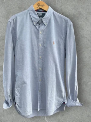 Grå skjorta Polo Ralph Lauren slim fit - Klassisk ljusblå skjorta från Polo Ralph Lauren i slim fit med button-down krage och broderad logga på bröstet. Skjortan har långa ärmar och stängs med vita knappar framtill. Perfekt till jeans eller chinos för en clean look. Väldigt sparsamt använd, och endast använd ett få tal gånger sedan inköpt. Hör av er vid minsta fundering. :) 