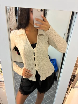 Beige kofta med struktur och knappar - Superfin beige kofta med strukturerat tyg och stora matchande knappar framtill. Koftan har lång ärm, krage och en figurnära passform. Perfekt att slänga över ett linne eller topp för en chill men ändå snygg look.