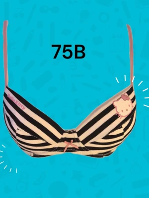 Hello Kitty randig bh 75B - Supersöt bh från Hello Kitty i svartvitt randigt med tunna rosa axelband. På ena kupan finns ett tryck av Hello Kitty med två hjärtan och en liten rosa rosett framtill. Perfekt för dig som gillar gulliga detaljer och lekfull stil. Varan är oanvänd och kommer från ett konkurslager från 2000-talet. I många fall är prislappen kvar (se bild). Har fler annonser och bra bundlerabatt vid köp av flera.