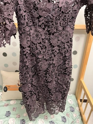 Lila spetsklänning med blommönster - Superfin lila klänning med detaljerad spets och blommönster. Klänningen har halv-långa ärmar och är knälång. Spetsen ger en lyxig känsla och blommorna gör den extra unik. Perfekt för dig som vill sticka ut med en elegant look.