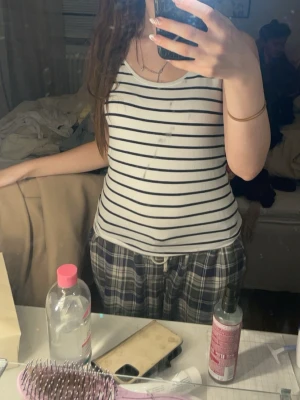 Randig vit linnetopp i bomull - Säljer en fräsch vit linnetopp med svarta horisontella ränder från C. Toppen är ärmlös och har en klassisk rund halsringning. Tillverkad i mjuk ekologisk bomull, perfekt för en chill och enkel stil.