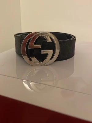 Svart Gucci skärp med GG-spänne - Säljer ett svart äkta Gucci skärp med klassiskt GG-mönster och stort silverfärgat GG-spänne. Skärpet är gjort i skinn och har en stilren look som passar till jeans eller kostymbyxor. Märkningen syns på insidan av lädret. 9/10 skick. Box ingår i köpet. Köpt för 4800kr på Guccis egna hemsida.