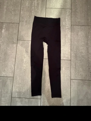 Svarta leggings - Säljer ett par svarta leggings med hög midja och diskret logga på benet. De är tillverkade i ett stretchigt syntetmaterial med lätt struktur och sitter tight. Perfekta för träning eller chill dagar.