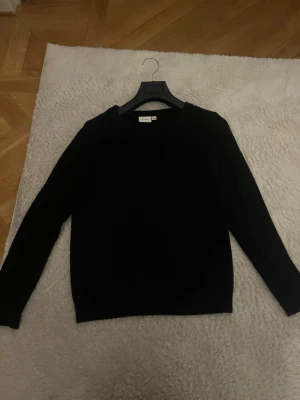 Svart stickad tröja från vila  - En stilren svart stickad tröja från vila med rund halsringning och långa ärmar. Tröjan har en klassisk passform och är perfekt för lager-på-lager. Materialet  är  mjukt och bekvämt, ull och  bomulls material! 