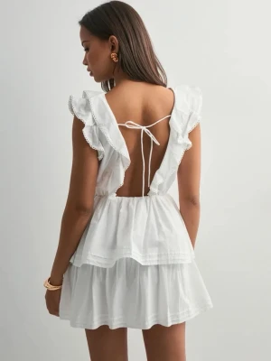 Vit volangklänning med öppen rygg - Söt vit kortklänning med volangdetaljer och v-ringning. Klänningen har öppen rygg med knytband och är ärmlös med volangprydda axlar. Perfekt för sommarens alla tillfällen.