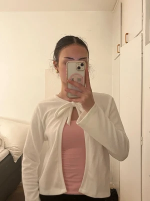 Vit kofta med knytning fram - Söt vit kofta med knytning framtill och långa ärmar. Koftan har en mjuk och lätt struktur, perfekt att slänga över ett linne eller topp. Enkel och stilren design som passar till många outfits.