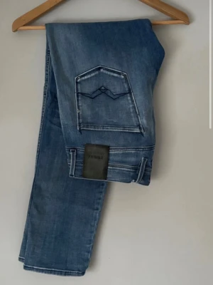 Replay Anbass blå jeans herr - Säljer ett par snygga Replay Anbass jeans i klassisk blå tvätt. Jeansen har fem fickor, raka ben och tydliga sömmar på bakfickorna. Materialet är mjukt jeans-tyg i bomull med lite stretch för extra komfort. Perfekta till vardagslooken!