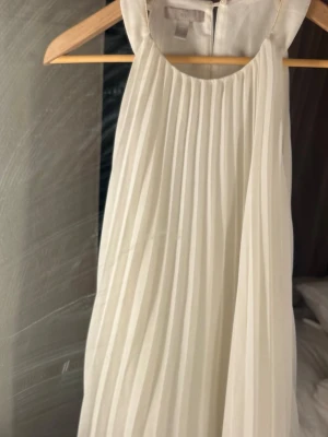Vit plisserad klänning/blus  från H&M - Från H&M i storlek M. Klänningen/blusen har ett plisserat tyg, är ärmlös och har en rund halsringning. Halsringen har sminkfläck , ej testat med fläckborttagning 