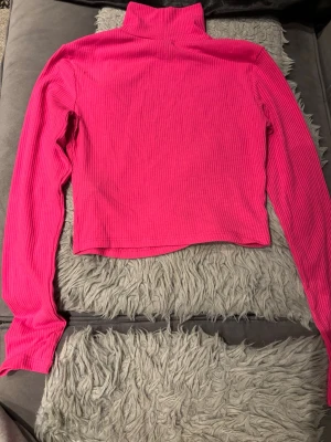 Rosa ribbad polotopp från H&M Divided - Snygg croppad polotopp i starkt rosa från H&M Divided. Toppen är ribbad, har lång ärm och hög krage. Perfekt att styla med jeans eller kjol för en trendig look.