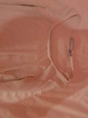 Ljusbeige ribbad långärmad topp - Superfin ljusbeige långärmad topp från Gina Tricot med ribbad struktur och lätt croppad passform. Toppen har en rundad halsringning och vågig kant nertill som ger en söt touch. Perfekt att styla med jeans eller kjol.