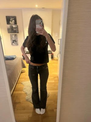Mörkgrå bootcut jeans - Säljer ett par mörkgrå bootcut jeans med låg midja. Jeansen har klassisk femficksdesign och är tillverkade i ett mjukt jeansmaterial. Snygg passform som sitter tajt upptill och släpper ut vid benen. Perfekta för dig som gillar en retroinspirerad look.