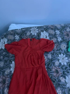 Röd omlottklänning från SHEIN - Trendig röd omlottklänning från SHEIN i storlek S. Klänningen har korta puffärmar, markerad midja och en lätt utställd kjol. Tillverkad i ett mjukt, vävt material som ger en snygg siluett. Perfekt för dig som vill sticka ut med färg!