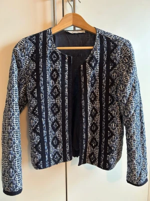 Mango Blå Kviltad Boho-jacka - Snygg cardigan jacka med blått och vitt mönster och svarta detaljer. Jackan har rund halsringning, lång ärm och är quiltad för extra stil. Riktigt snygg "boho möter business"-vibe! 💙 