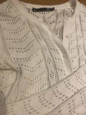 Vit stickad kofta med hålmönster - Snygg vit stickad kofta från 157 med hålmönster och rund hals. Koftan har knappar. Perfekt att slänga över en topp för en stilig elegant look.