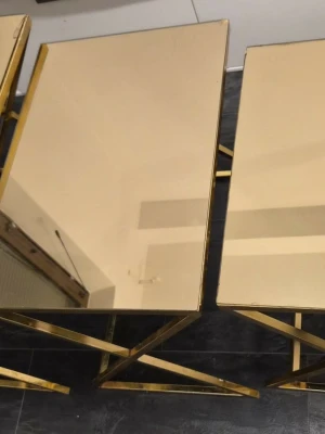 Guldiga sidobord med spegelyta - Två stilrena sidobord med spegelyta och guldfärgade metallramar. Bordens design är modern med raka linjer och reflekterande yta som ger en lyxig känsla till rummet. Perfekta som avlastningsbord eller dekorativa ytor.