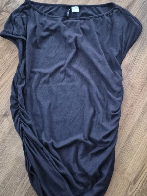 Svart omlott topp med rynkade detaljer på sidorna - Svart topp från HM i mjukt bomullsmaterial. Modellen är loose fit med korta ärmar och har rynkade detaljer på sidorna som ger en snygg draperad effekt. 