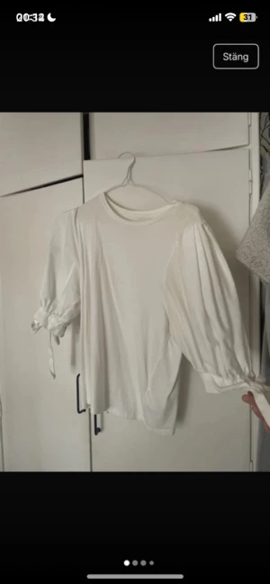 Vit blus med puffärm och knytband - Säljer en vit blus med puffiga trekvartsärmar och fina knytband vid ärmsluten. Blusen har rund halsringning och är gjord i ett mjukt, vävt material som känns skönt mot huden. Perfekt för dig som gillar en stilren men ändå trendig look.